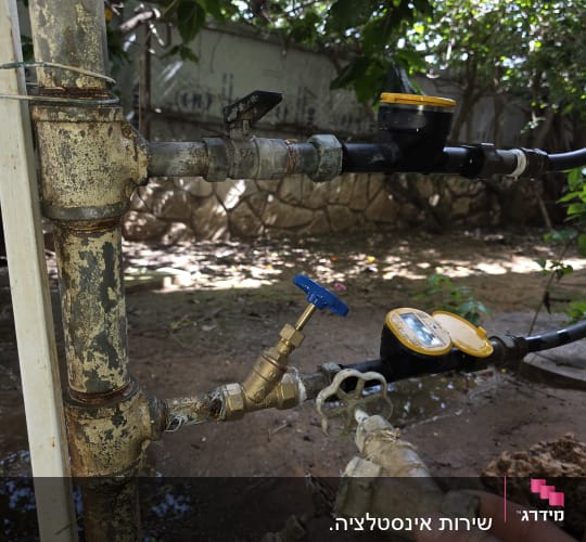 צנרת מים עם ברזים ומד מים בגינה